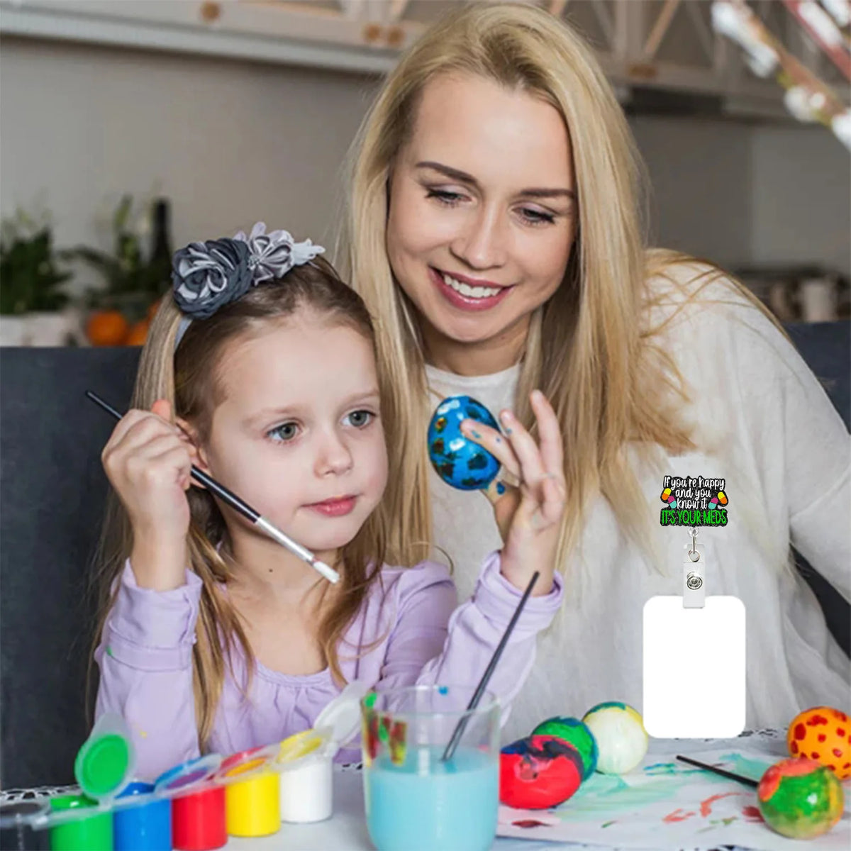 Eine blonde Frau hält die Hand eines jungen Mädchens, während sie bunte Glitzerartikel auf einem Tisch anschauen.