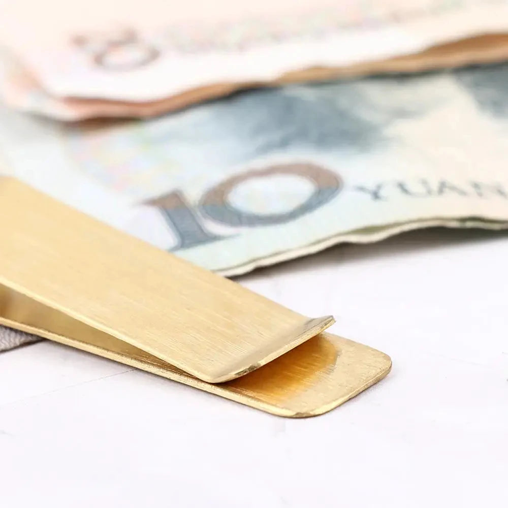 A vintage solid brass money clip with a card holder resting on a blurred background of currency.