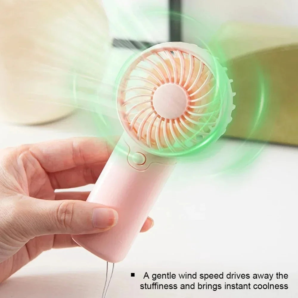 A hand holds a pink portable rechargeable mini handheld fan with a green spinning blade, demonstrating its cooling function.