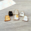 Una colección de cinco pines de esmalte con gatos lindos en varios colores y estilos
