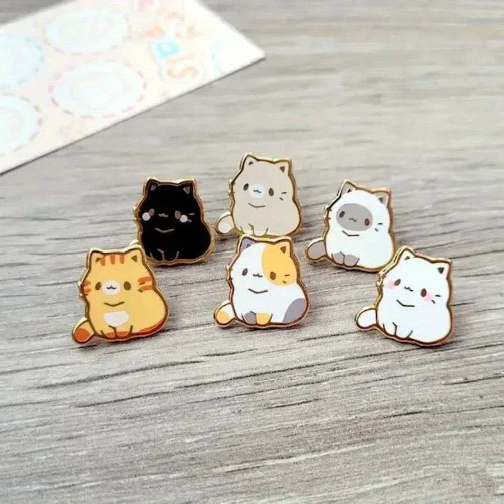 Una colección de cinco pines de esmalte con gatos lindos en varios colores y estilos