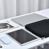 Una laptop plateada junto a una funda negra y un iPad de Apple con un mouse blanco sobre una mesa blanca.