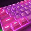 A close-up view of a pink backlit mechanical keyboard keycaps showing various letters and function keys.
