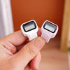 A hand holds a pink digital counter device with a white casing and a black display.