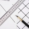 A black pen is placed next to a stainless steel measuring ruler marked in millimeters on white paper.
