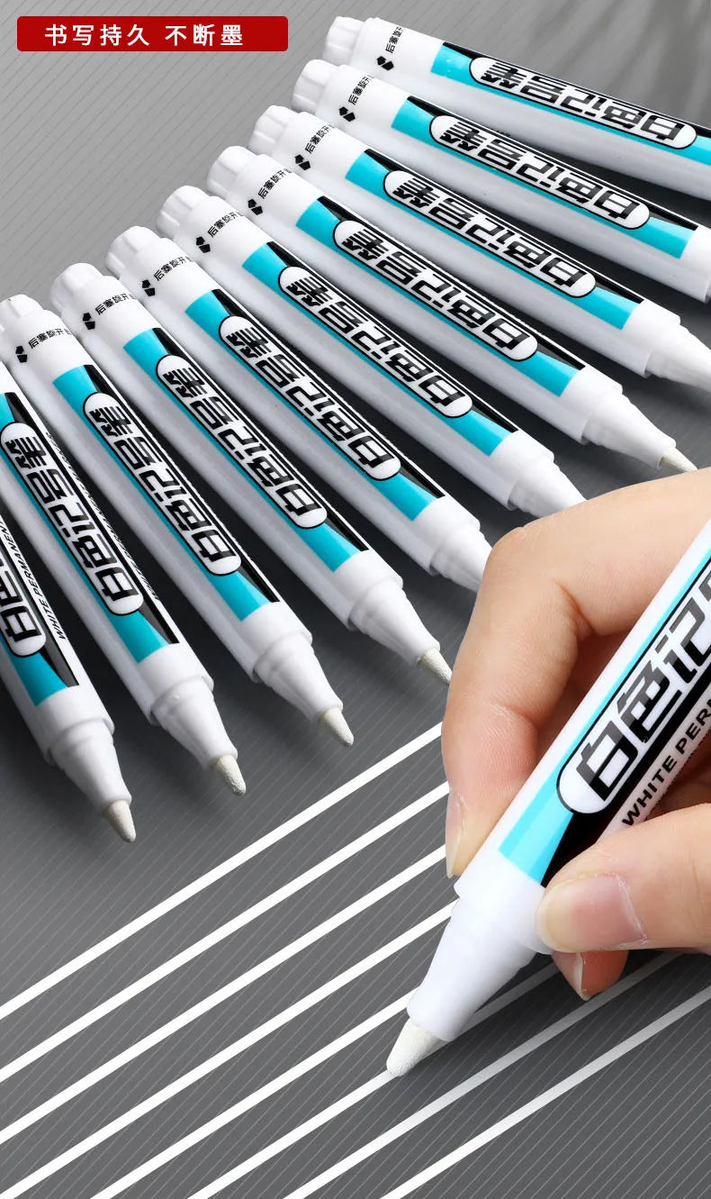 A hand holds a white permanent paint marker pen with blue accents, showing the tip and barrel.