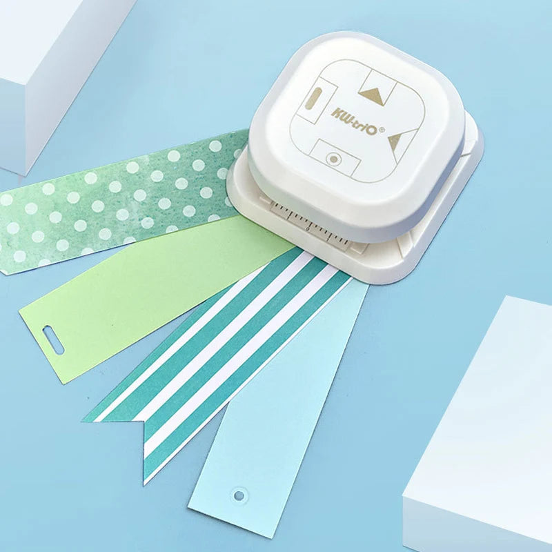 A white crafting tool with a ruler and punch is shown next to several colored paper strips on a light blue background.
