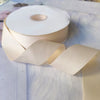 Roll of matte finish satin ribbon in a pale beige color lying on a white surface.