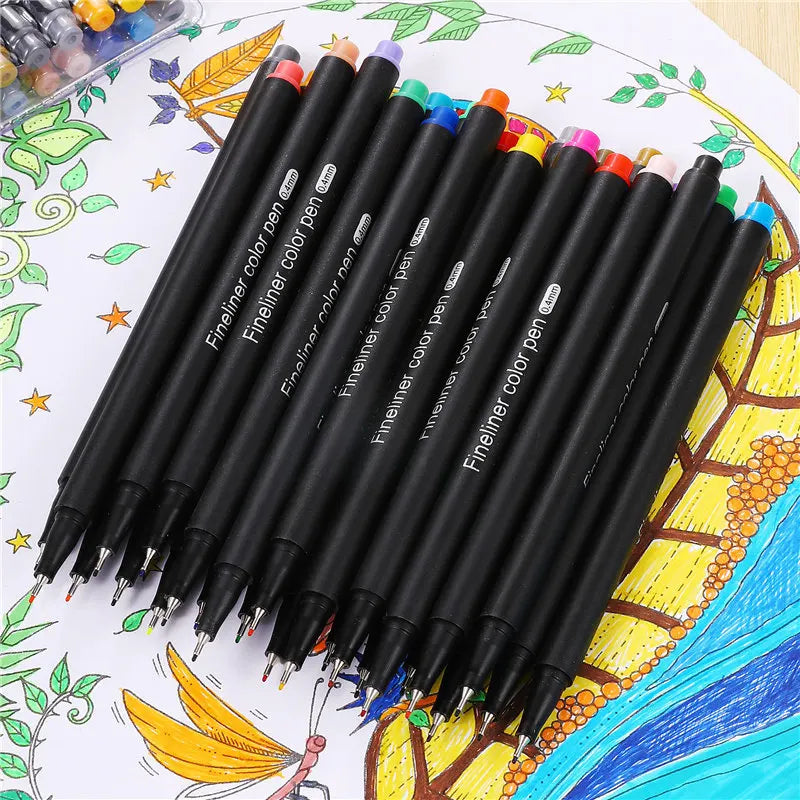 A set of fine line marker pens in various colors, including black and purple, laid out on a sheet of paper with botanical ill