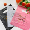 Pink thank you gift bag with handle and a black bag next to it, surrounded by orange flowers.