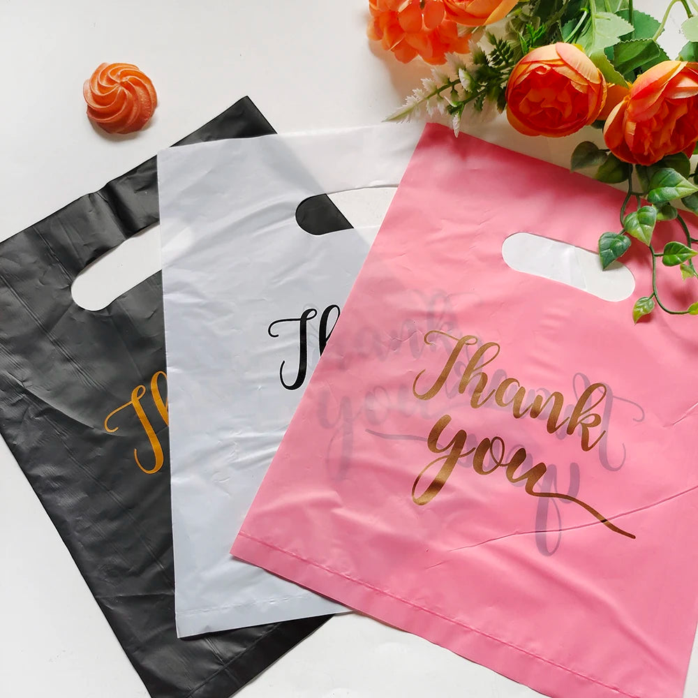 Pink thank you gift bag with handle and a black bag next to it, surrounded by orange flowers.