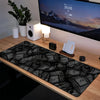 A large black and white desk mat with a pattern of stacked money is placed on a wooden desk in front of a computer monitor.