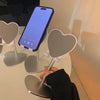 A hand is adjusting an adjustable desktop phone and tablet stand with a silver base and heart-shaped holders.