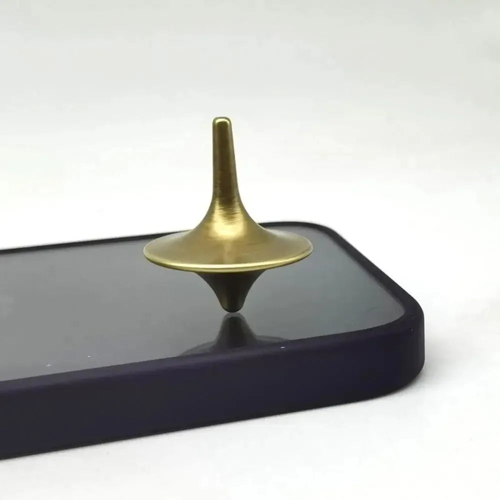 A brass metal hand spinning top fidget toy resting on a dark surface.