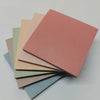 Ein Stapel bunter quadratischer Klebeflister in verschiedenen Rosa-, Beige- und Grüntönen.