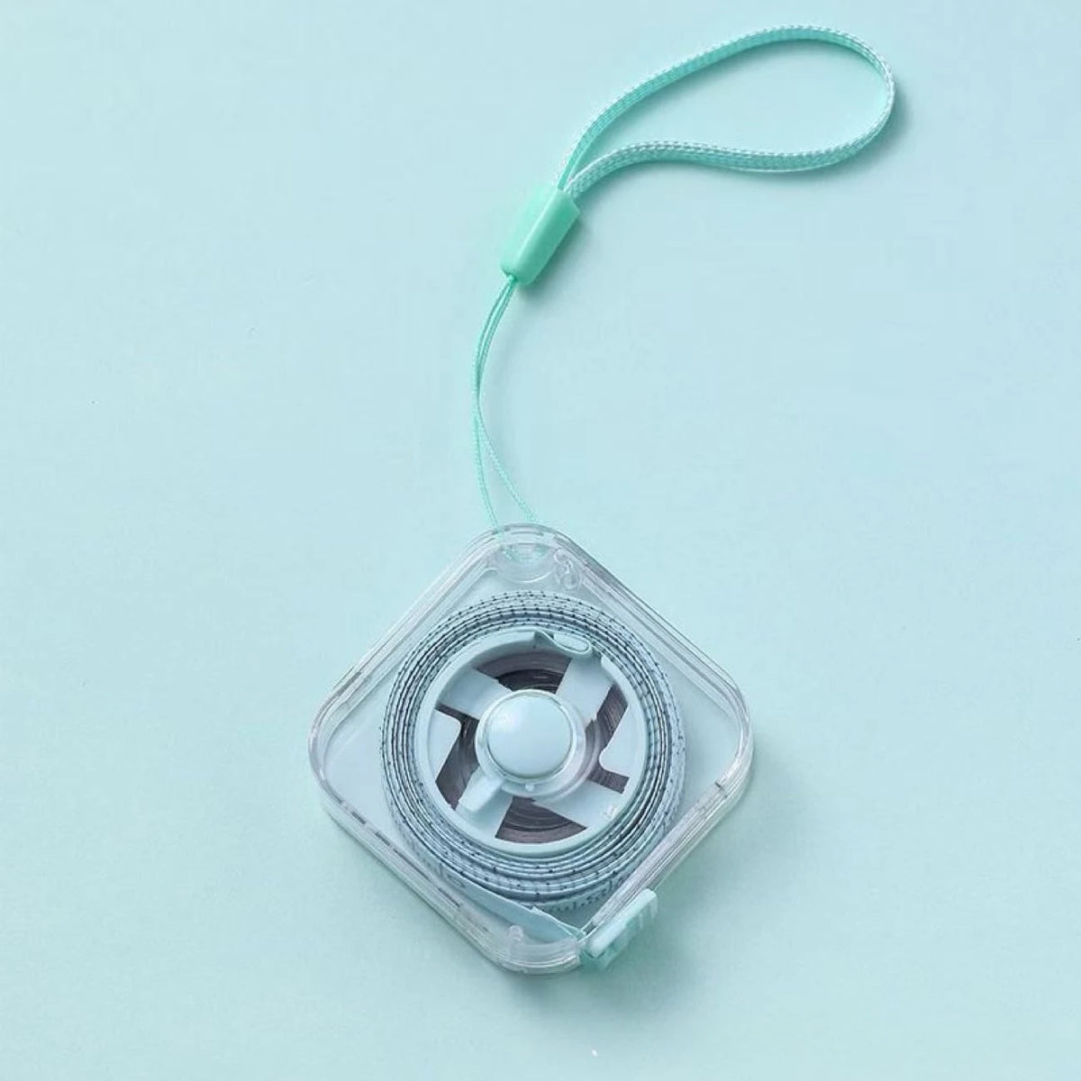 A clear plastic compact retractable measuring tape with a green cord is shown against a light blue background.
