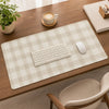 A beige plaid pattern non-slip mouse pad is placed on a wooden desk next to a laptop and a coffee cup.