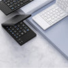 A black foldable Bluetooth keyboard and a white laptop keyboard are displayed on a gray surface.