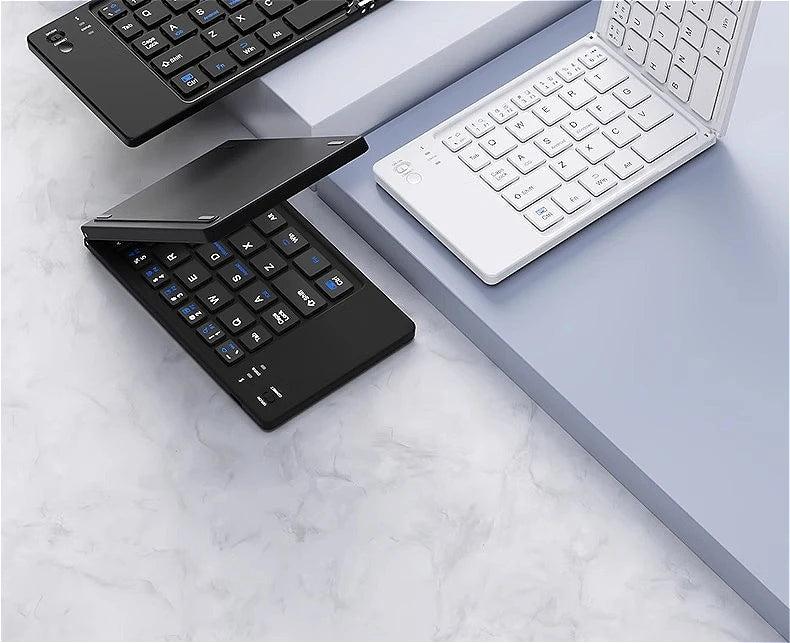 A black foldable Bluetooth keyboard and a white laptop keyboard are displayed on a gray surface.