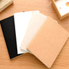 A set of four A6 blank sketchbooks in black, white, beige, and tan resting on a wooden surface.