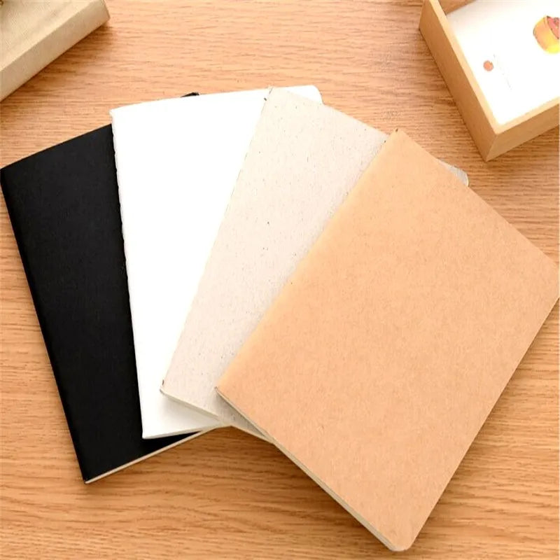A set of four A6 blank sketchbooks in black, white, beige, and tan resting on a wooden surface.
