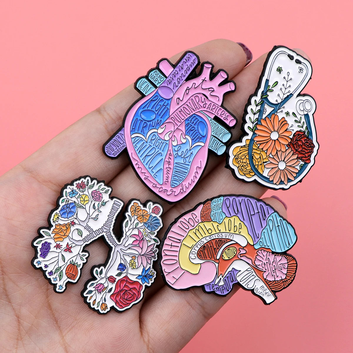 A hand holds several enamel pins featuring medical themes like a heart, lungs, and brain.