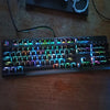 A close-up shot of a black mechanical keyboard with colorful RGB backlighting resting on a wooden surface.
