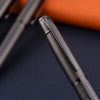 A close-up view of a black metal ballpoint pen with a textured grip and smooth barrel, resting on a dark surface.