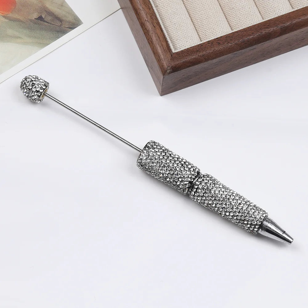 A silver pen accessory featuring a rhinestone ball and a beaded tip, displayed on a white surface.