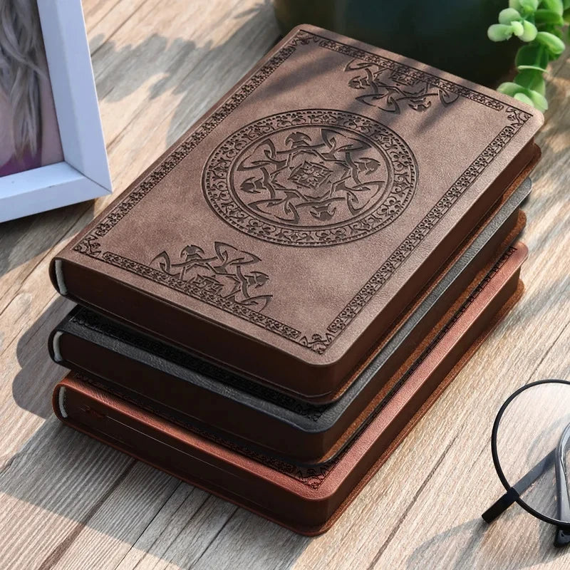 A stack of brown retro PU leather pocket notebooks with intricate embossed designs on a wooden surface.