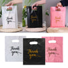 Three thank you gift bags in white, black, and pink with handles, shown being held by hands.
