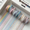A collection of pastel colored washi tape rolls displayed on a white box for crafting and decoration.