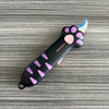 A black utility knife shaped like a cat paw with purple accents and a light blue blade resting on a gray wooden surface.