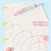 A set of four pink heart-shaped gel pens with animal patterns are shown writing on lined paper.