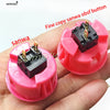 A hand holds a pink arcade push button with a black micro switch and a gold pin.