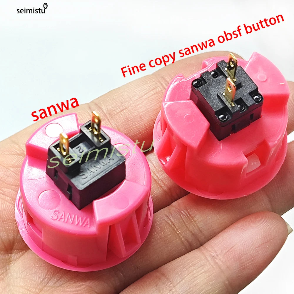 A hand holds a pink arcade push button with a black micro switch and a gold pin.
