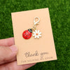 A thank you card with a ladybug and daisy keychain set resting on green grass.