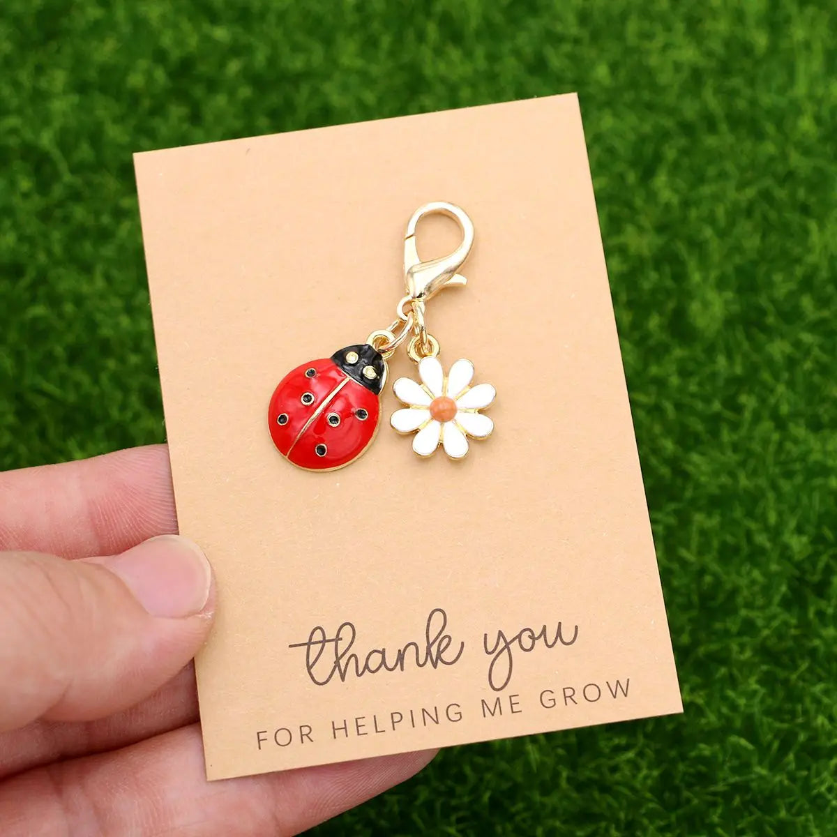 A thank you card with a ladybug and daisy keychain set resting on green grass.