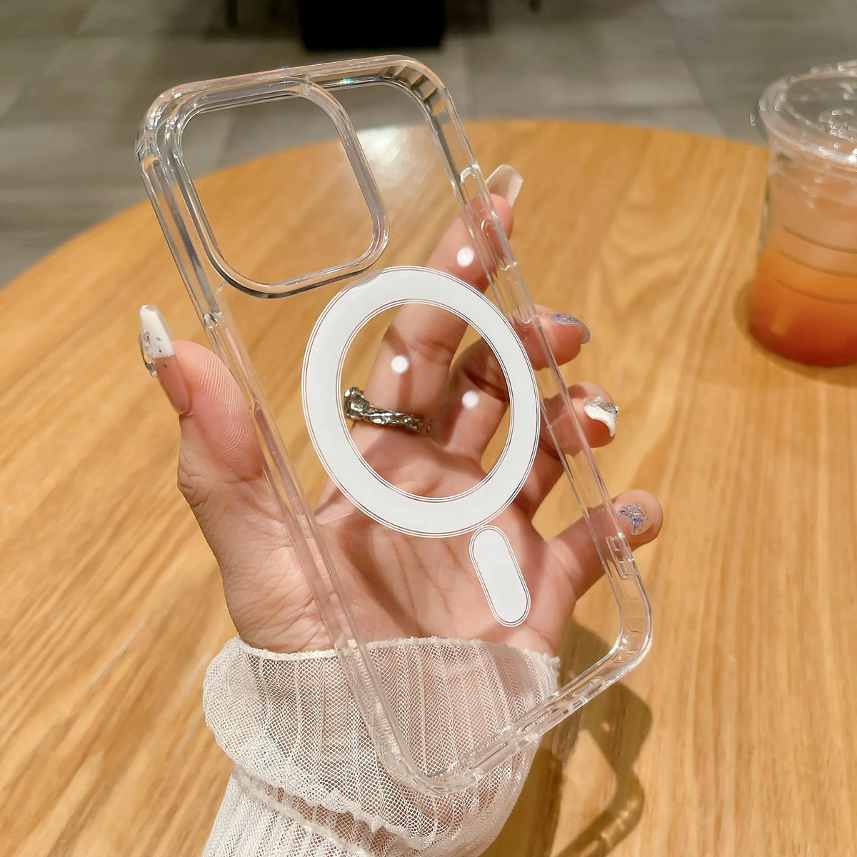A hand holds a clear magnetic phone case with built-in magsafe compatibility on a wooden table.