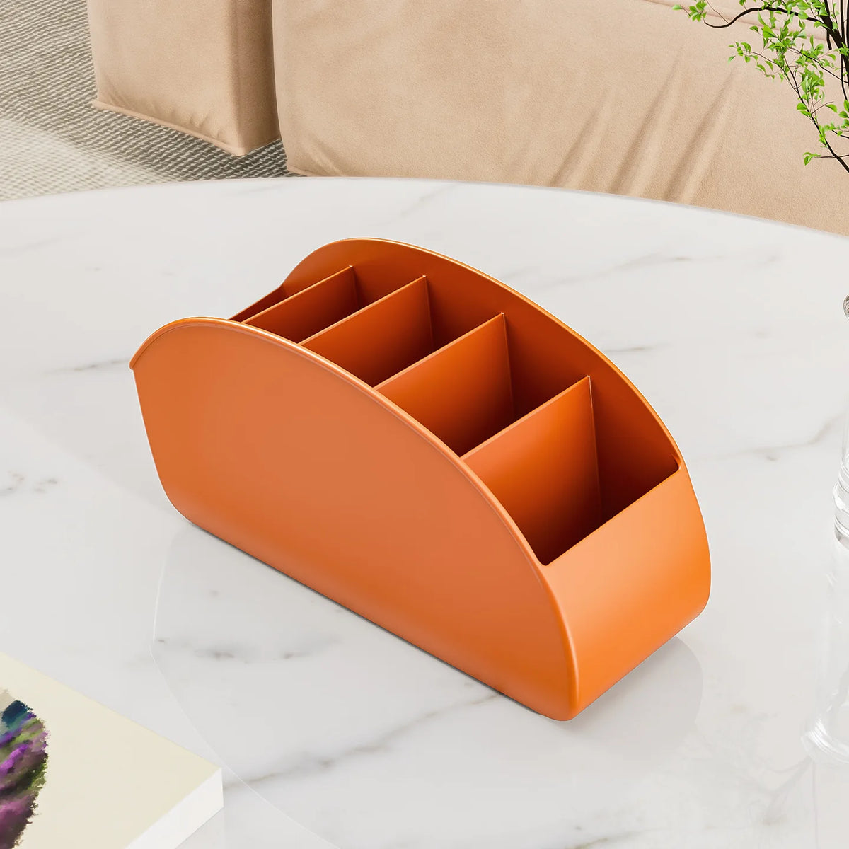 An orange plastic remote control holder and desk organizer tray resting on a white marble surface.