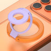 A purple phone ring holder stand is shown resting on an orange surface next to a charging pad.