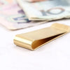 A vintage solid brass money clip with a card holder lying on a white surface next to some paper currency.