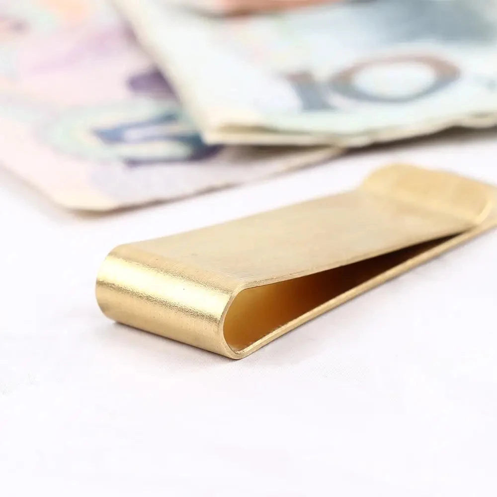 A vintage solid brass money clip with a card holder lying on a white surface next to some paper currency.