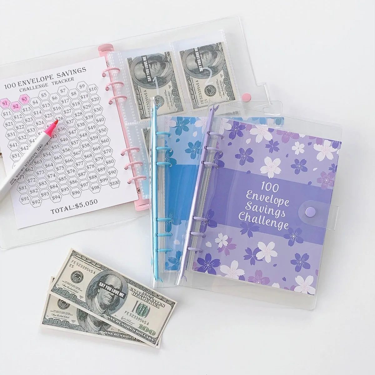 A set of 100 envelope savings challenge trackers and a stack of US dollar bills are displayed on a white background.