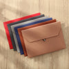 A stack of leather document organizer bags in various shades of red, blue, gray, and pink resting on a wooden surface.