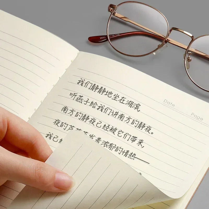 A close-up of an open A5 Kraft cover notebook showing handwritten Chinese text and a pair of eyeglasses.