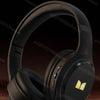 Black over-ear headphones with a gold accent, shown against a dark background.