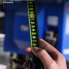 A hand holds a fluorescent steel tape measure, demonstrating its ability to measure three meters without bending.