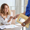A woman is handing a kraft paper bubble mailer to another person in an office setting.