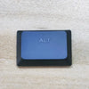 A dark blue replacement keycap labeled ALT resting on a light beige fabric surface.